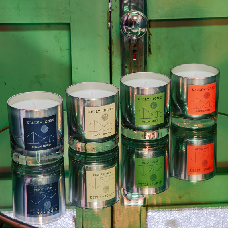 The full set of K+J Eau de Mezcal Candles, Blanca, Negra, Roja and Verde, in a mezcal bar in Oaxaca on a glass table with a green door in the background.