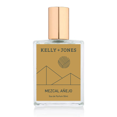 A bottle of Kelly + Jones MEZCAL AÑEJO Eau de Parfum Spray with a gold-colored label and cap, set against a white background.