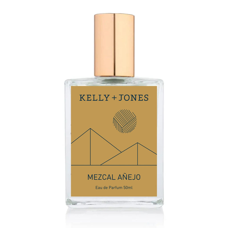 A bottle of Kelly + Jones MEZCAL AÑEJO Eau de Parfum Spray with a gold-colored label and cap, set against a white background.