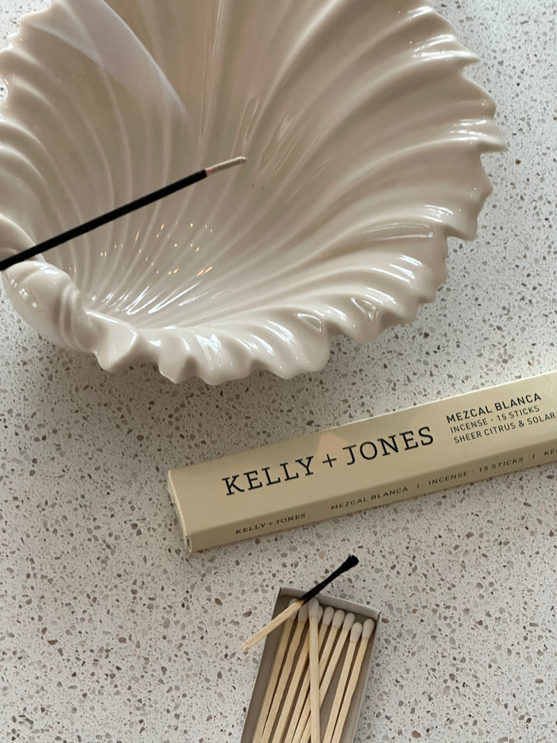 White shell-shaped incense burner with a matchbox and matches on a speckled surface, featuring Kelly + Jones Mezcal Blanca Incense