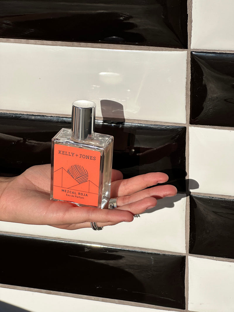 Hand holding a perfume bottle with an orange label against a black and white checkered background